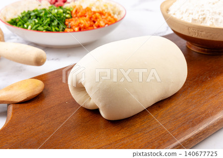 Fresh raw wheat dough on wooden cutting board for making traditional Chinese dumplings Fresh raw wheat dough on wooden cutting board for making traditional Chinese dumplings 140677725