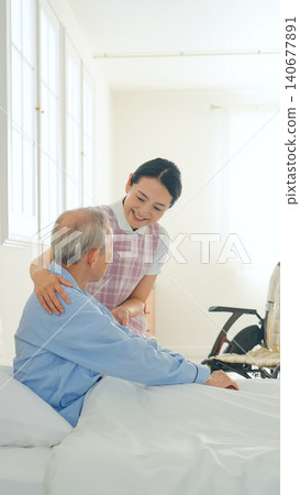 Female care staff supporting a senior man in bed 140677891