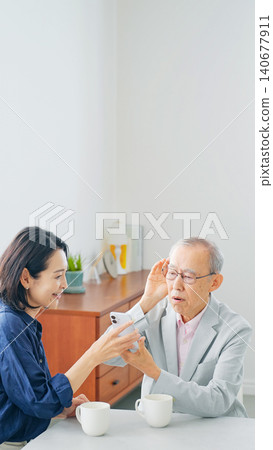 A senior man and a middle-aged woman talking while looking at their smartphones. A senior man and a middle-aged woman talking while looking at their smartphones. 140677911