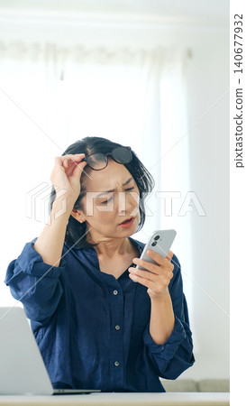 A middle-aged woman worries while looking at her smartphone A middle-aged woman worries while looking at her smartphone 140677932