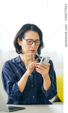 A middle-aged woman worries while looking at her smartphone A middle-aged woman worries while looking at her smartphone 140677933