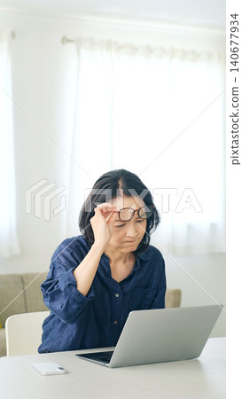 一位女士摘下眼鏡,看著電腦螢幕。 一位女士摘下眼鏡,看著電腦螢幕。 140677934