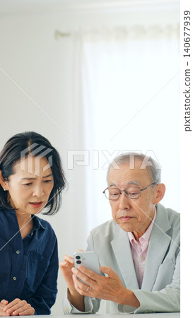 A woman and a senior man looking at their smartphones and contemplating something. A woman and a senior man looking at their smartphones and contemplating something. 140677939