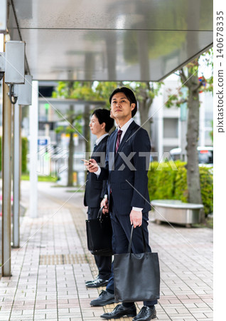 A man in a suit waiting for a bus at a bus stop. A man in a suit waiting for a bus at a bus stop. 140678335