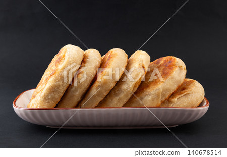 A row of golden fried meat pies served on a long ceramic plate against a dark background. 140678514