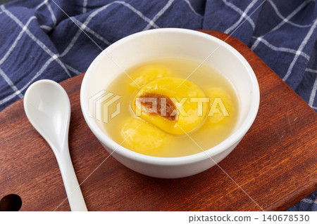 Yellow glutinous rice balls filled with brown sugar filling served in a traditional bowl on a wooden tray. 140678530