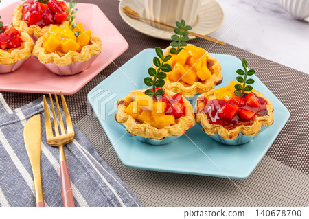 flaky croissant egg tarts topped with fresh mango cubes, strawberries, and glaze,on plate. 140678700