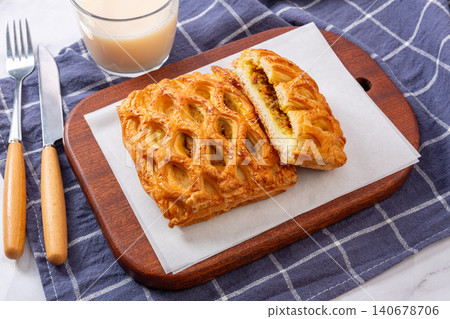 High angle view of golden curry chicken lattice pies served on a wooden cutting board with a glass of milk and cutlery. High angle view of golden curry chicken lattice pies served on a wooden cutting board with a glass of milk and cutlery. 140678706