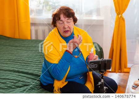 Caucasian grandmother creating beauty related content while reviewing personal care products. Influencer concept. Comfortable indoor environment and retirement. Mid shot Caucasian grandmother creating beauty related content while reviewing personal care products. Influencer concept. Comfortable indoor environment and retirement. Mid shot 140678774