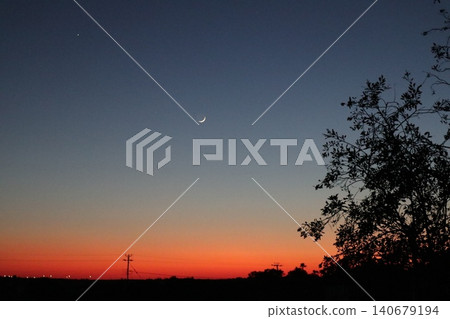 A thin, new moon in a cloudless evening sky. A beautiful blue-orange sky at sunset. A thin, new moon in a cloudless evening sky. A beautiful blue-orange sky at sunset. 140679194