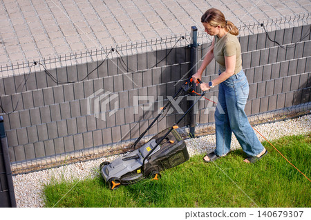 Woman mowing lawn with electric mower in small garden Woman mowing lawn with electric mower in small garden 140679307