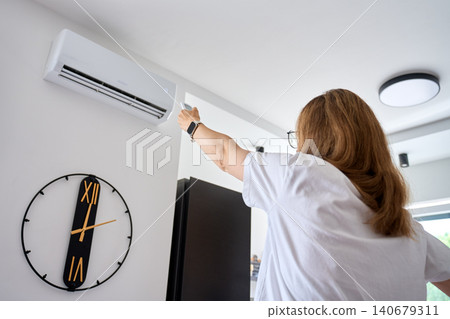 Woman turning on air conditioner with remote control 140679311