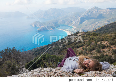 Young woman lying on high cliff over Oludeniz beach, Lycia coast. Summer day walk by Lycian way at family vacation in Mediterranean Sea, Fethye, Antalya region, Turkey Young woman lying on high cliff over Oludeniz beach, Lycia coast. Summer day walk by Lycian way at family vacation in Mediterranean Sea, Fethye, Antalya region, Turkey 140679721