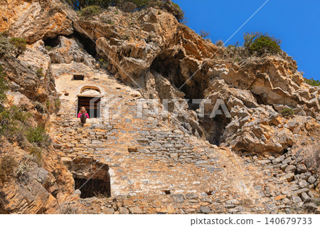 Woman looking at beautiful view from window of Afkule monastery carved into high vertical cliffs near Oludeniz, Turkey. Dramatic rock landscape and historic architecture. Travel, cultural destination. Woman looking at beautiful view from window of Afkule monastery carved into high vertical cliffs near Oludeniz, Turkey. Dramatic rock landscape and historic architecture. Travel, cultural destination. 140679733