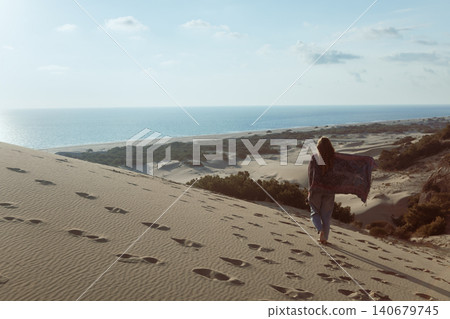 Woman walks along golden sand dunes at Patara Beach, Turkey, enjoying open space and sea views. Inspiring travel moment highlighting freedom, exploration and coastal tourism. Woman walks along golden sand dunes at Patara Beach, Turkey, enjoying open space and sea views. Inspiring travel moment highlighting freedom, exploration and coastal tourism. 140679745