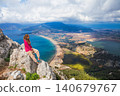 Woman sits on a rocky cliff above Dalyan, Turkey, overlooking sea,  Iztuzu Turtle beach, river delta and lagoon. Inspiring travel scene with panoramic coastal landscape and outdoor lifestyle. 140679767