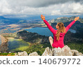 Woman sits on high cliff with raised hands overlooking Dalyan delta and Iztuzu Turtle Beach in Turkey. Inspiring travel moment symbolizing freedom, adventure and summer family tourism. 140679772