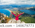 Woman sits on high cliff with raised hands overlooking Dalyan delta and Iztuzu Turtle Beach in Turkey. Inspiring travel moment symbolizing freedom, adventure and summer family tourism. 140679773