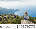 Young boy sits on a rocky viewpoint overlooking the sea in Turkey. Calm travel moment with wide coastal landscape, inspiring exploration and outdoor family adventure. 140679775