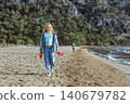 Girl walks barefoot along Iztuzu Beach near Dalyan, Turkey, holding her sandals. Relaxed summer travel moment with sandy coast, sea breeze and active outdoor lifestyle. 140679782