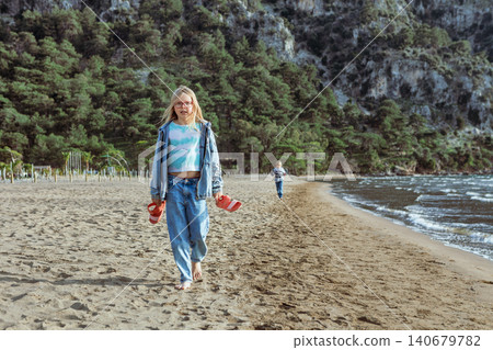 Girl walks barefoot along Iztuzu Beach near Dalyan, Turkey, holding her sandals. Relaxed summer travel moment with sandy coast, sea breeze and active outdoor lifestyle. 140679782
