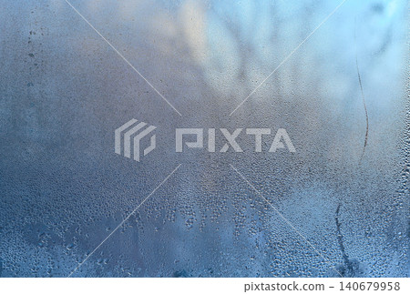 Close-up of condensation on a glass window, showing moisture accumulation on the surface and forming water droplets. blue background of wet glass. Close-up of condensation on a glass window, showing moisture accumulation on the surface and forming water droplets. blue background of wet glass. 140679958