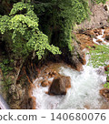 A natural landscape of a mountain stream and a clear stream flowing over rocky areas, surrounded by fresh greenery. 140680076