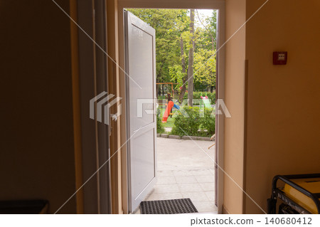 Open white door leading to a sunny outdoor playground with colorful slides and green trees in the backyard. Open white door leading to a sunny outdoor playground with colorful slides and green trees in the backyard. 140680412