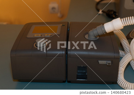 Modern portable medical device for respiratory therapy with digital screen and tubing on blue surface. Modern portable medical device for respiratory therapy with digital screen and tubing on blue surface. 140680423