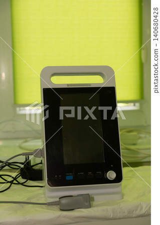 Portable medical ventilator monitor on hospital bed in bright green clinical room, minimal modern equipment 140680428