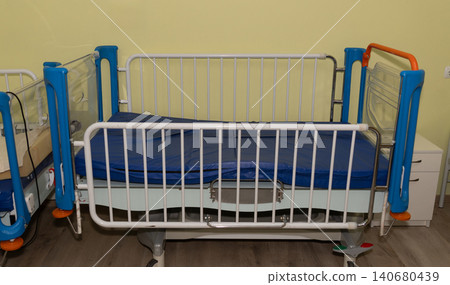 Empty medical hospital bed with blue mattress and white side rails in a clean clinical setting. 140680439