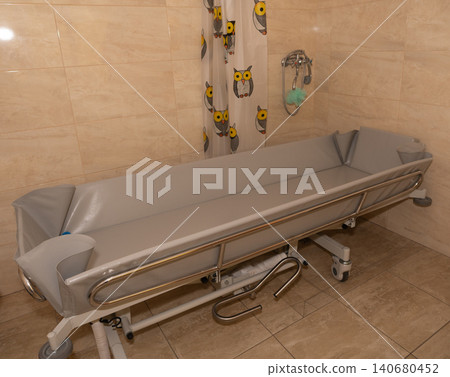 Medical stretcher bed with gray padded mattress and side rails in clinical shower room setting. Medical stretcher bed with gray padded mattress and side rails in clinical shower room setting. 140680452