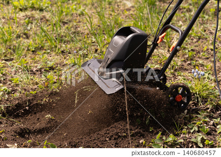 Electric garden tiller machine tilling soil in backyard garden during spring planting season. Electric garden tiller machine tilling soil in backyard garden during spring planting season. 140680457