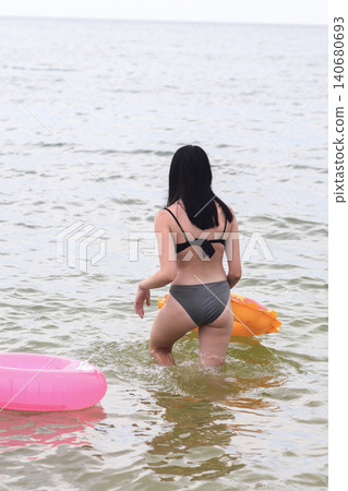 woman in a bikini walking in water at beach, enjoying warm summer day. 140680693