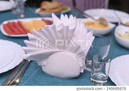 Napkin holder with folded white napkins placed on table setting. Napkin holder with folded white napkins placed on table setting. 140680878