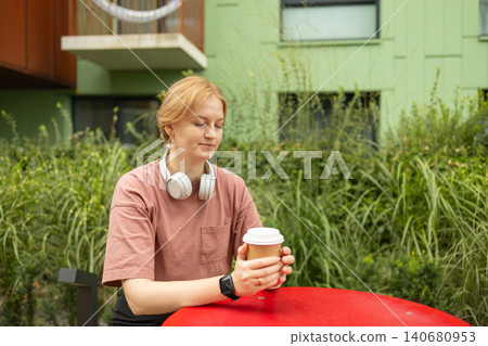 Smiling young woman holding coffee cup at outdoor terrace table Smiling young woman holding coffee cup at outdoor terrace table 140680953
