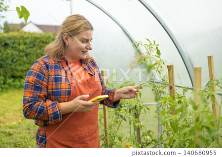 Young woman farmer working with smartphone in greenhouse garden Young woman farmer working with smartphone in greenhouse garden 140680955
