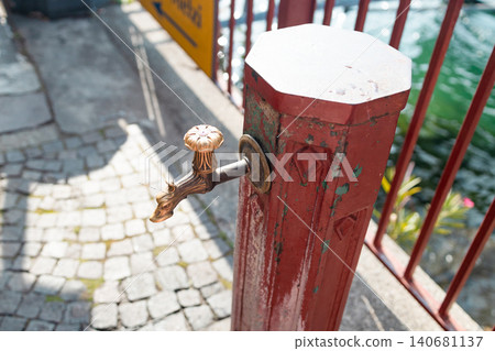 Vintage red public drinking water fountain on a cobblestone European street Vintage red public drinking water fountain on a cobblestone European street 140681137