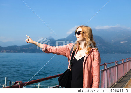 Young female tourist pointing at beautiful mountain lake view during summer vacation Young female tourist pointing at beautiful mountain lake view during summer vacation 140681143