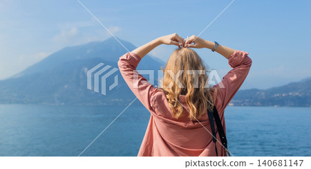 Female traveler showing heart gesture with hands looking at beautiful landscape background Female traveler showing heart gesture with hands looking at beautiful landscape background 140681147