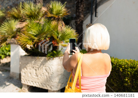 Back view of a blonde woman tourist taking a photo on a smartphone Back view of a blonde woman tourist taking a photo on a smartphone 140681181