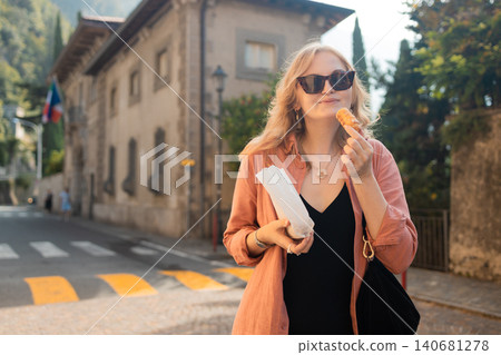 Young blonde woman eating traditional cookie on a city street Young blonde woman eating traditional cookie on a city street 140681278