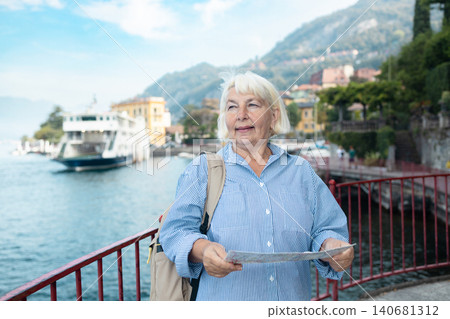 Happy senior woman tourist with a map at Lake Como Happy senior woman tourist with a map at Lake Como 140681312