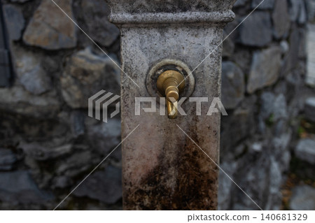 Old brass water tap on a stone fountain Old brass water tap on a stone fountain 140681329