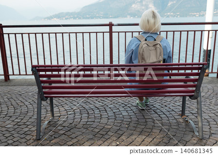Senior woman tourist relaxing on bench near mountain lake Senior woman tourist relaxing on bench near mountain lake 140681345