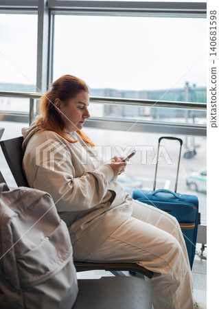 Young woman traveler sitting in airport waiting area and using smartphone Young woman traveler sitting in airport waiting area and using smartphone 140681598