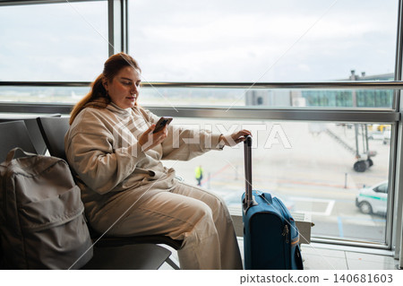 Young woman traveler sitting in airport waiting area and using smartphone Young woman traveler sitting in airport waiting area and using smartphone 140681603
