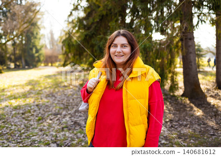 Happy young woman standing in park, smiling at camera, casual lifestyle portrait, outdoor scene with natural light and relaxed mood. Happy young woman standing in park, smiling at camera, casual lifestyle portrait, outdoor scene with natural light and relaxed mood. 140681612