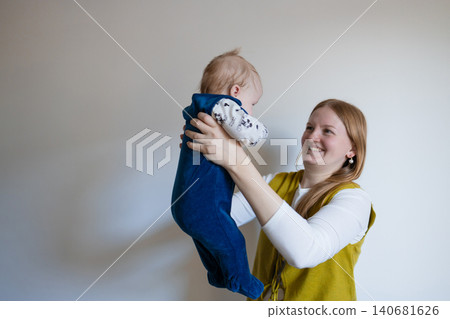 Happy young mother lifting her cute baby boy up in a bright room. Happy young mother lifting her cute baby boy up in a bright room. 140681626