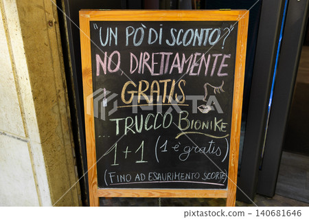 Handwritten chalkboard sign on street offering free promotion and discounts in Italian language. 140681646